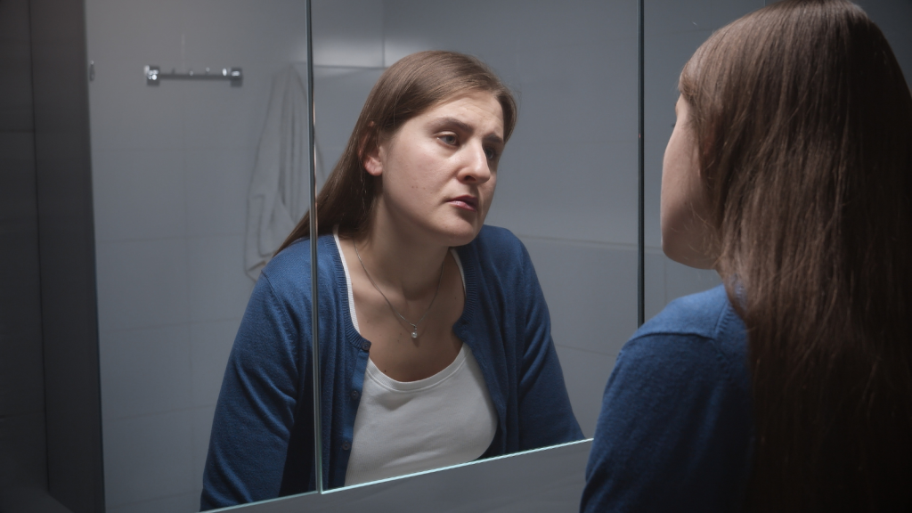 frustrated woman in bathroom looking in mirror