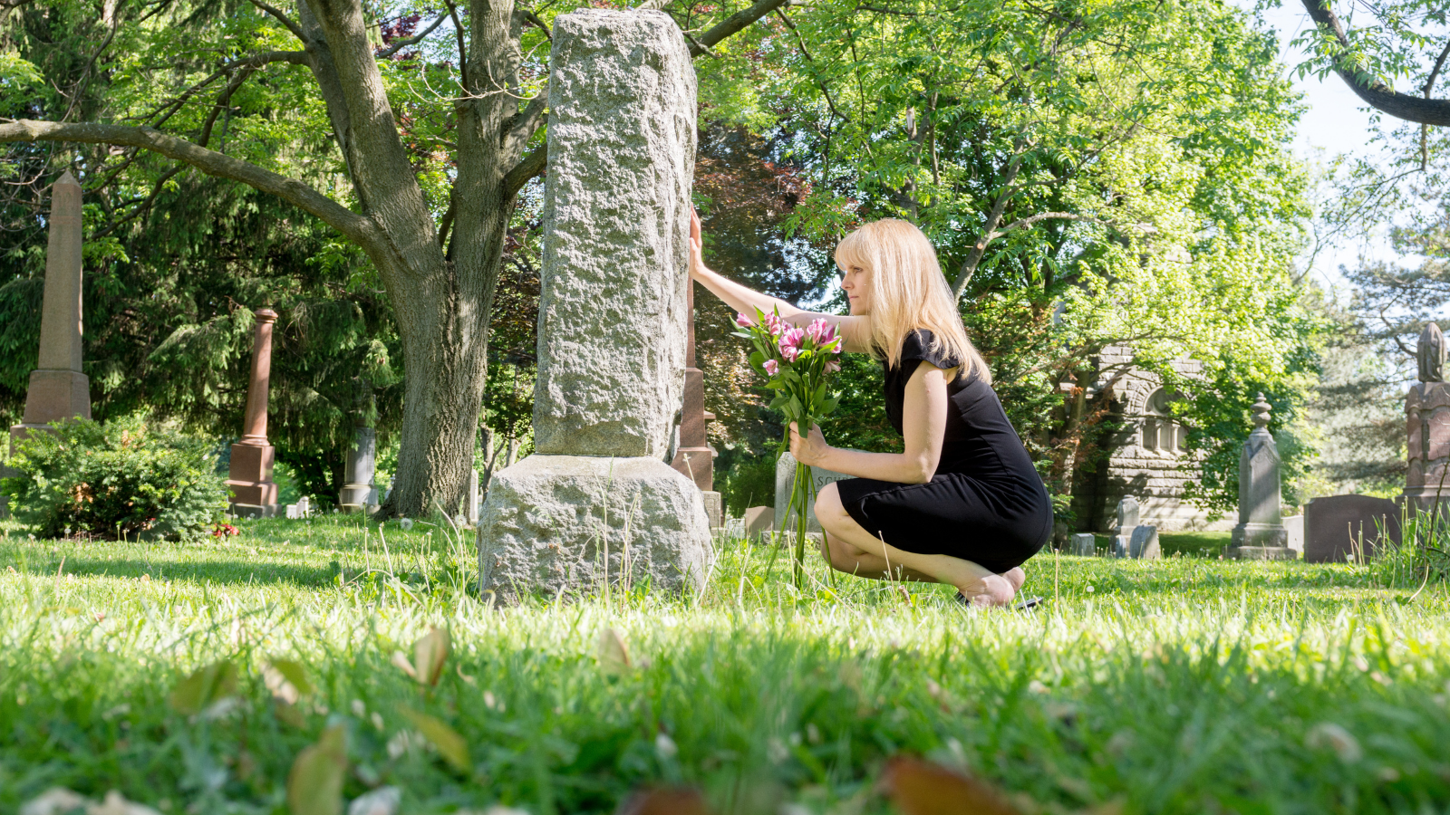 One Widow Received Everything After Her Husband’s Death, But A New Family Dispute Started When His Sister Asked Her To Divide The Inheritance grieving woman at grave headstone holding flowers
