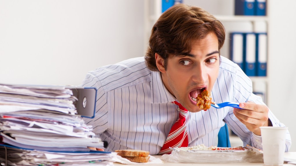 man furiously having lunch at his desk in the office