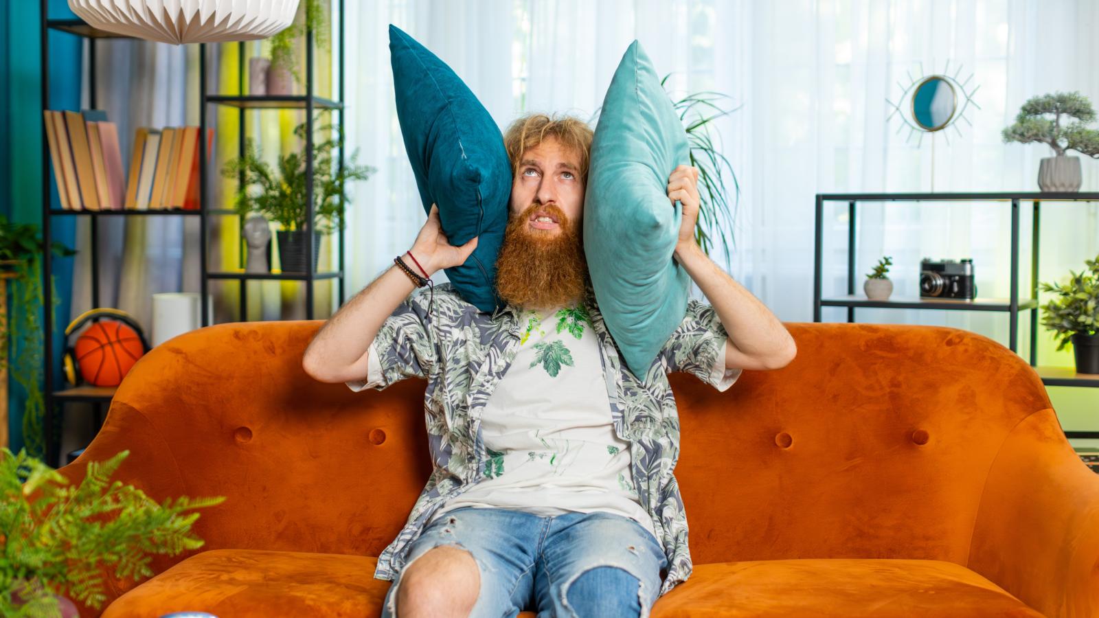 Man Just Moved Into A New Apartment, But His Neighbors Are Already Getting On His Nerves Because They Play Loud Music Late Into The Night man holding pillows to his ears
