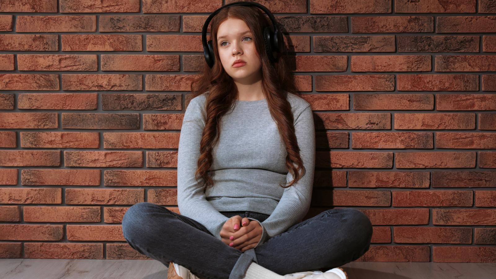 girl sitting against a brick wall
