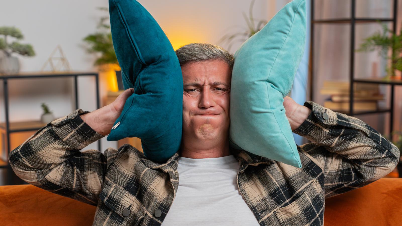 A Neighbors Open Door Turned the Hallway Into a Playroom—and One Resident Has Had Enough man plugging his ears with pillows