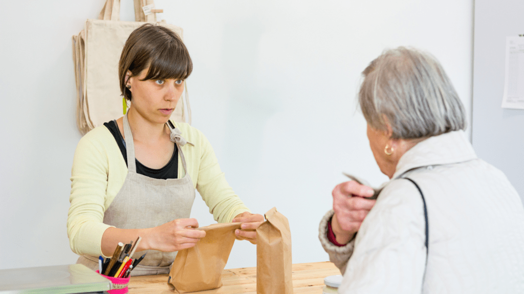 old woman customer and young woman cashier conversing over register and bag