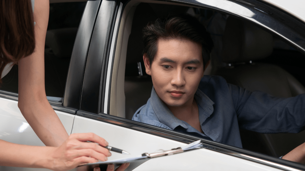 person with clipboard stopping asian man in car