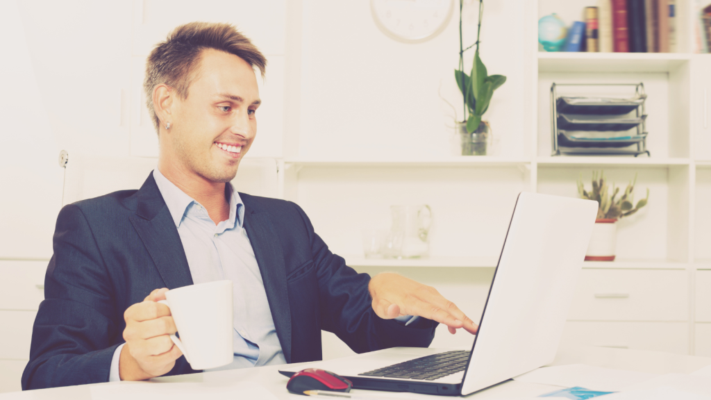 He Tried to Sound Smarter Than Everyone Else—Then Got Called Out for His Coffee Suggestion smiling businessman looking at computer with coffee in hand