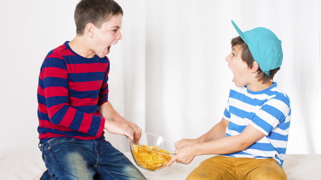 two young boys fighting over bowl of snacks