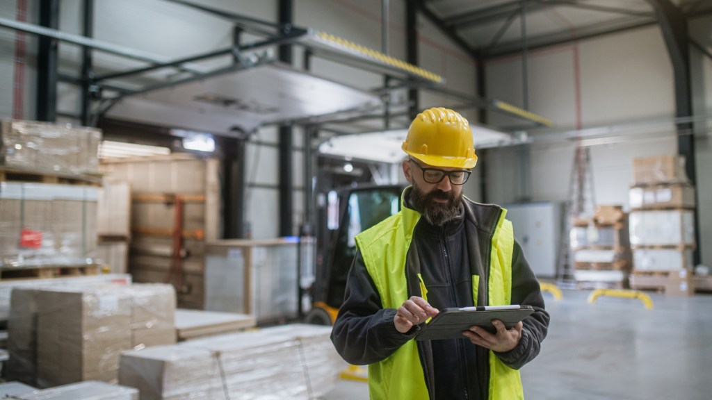 warehouse employee looking at paperwork wearing hard hat