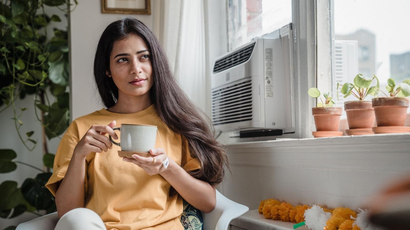 An Anxious Renter Is Convinced Her Air Conditioner Is Ruining Her Neighbor’s Life—Despite Zero Complaints woman sitting by her air conditioning unit