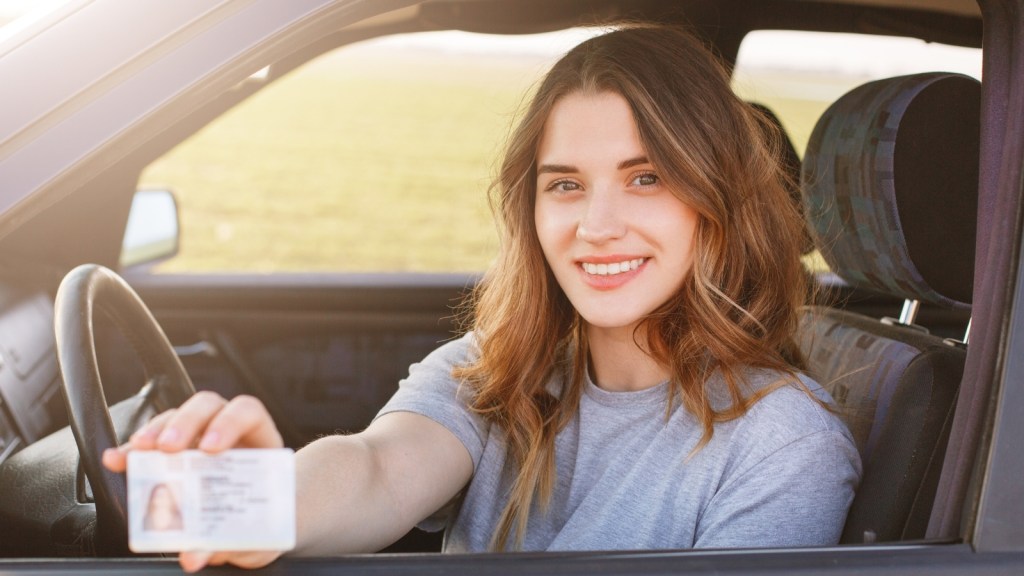 young woman in the car smiling with drivers license
