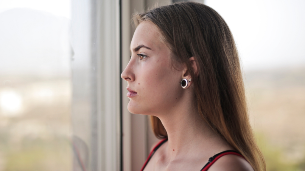 Her Family Expects Her To Join The Vacation, Yet The Hotel’s Bad Reviews Have Left Her Seriously Considering Staying Home Instead young woman looking out the window contemplating
