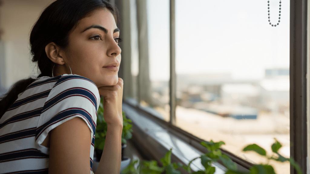 Asking For Help With Travel Costs Turned Into Family Drama When Her Mom And Sister Accused Her Of Being Manipulative About The Reunion young woman looking out window with chin resting on hand