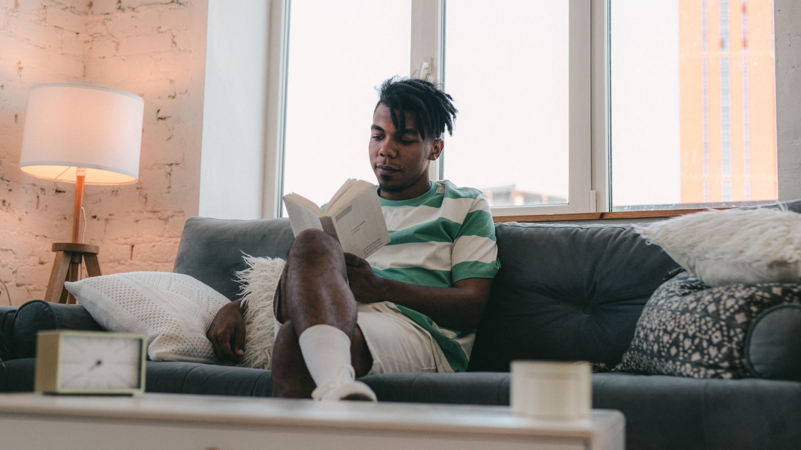 Man Moves Into His First Apartment—Then the Family Upstairs Starts Waking Him Up Early Every Morning Man sitting on his couch reading a book