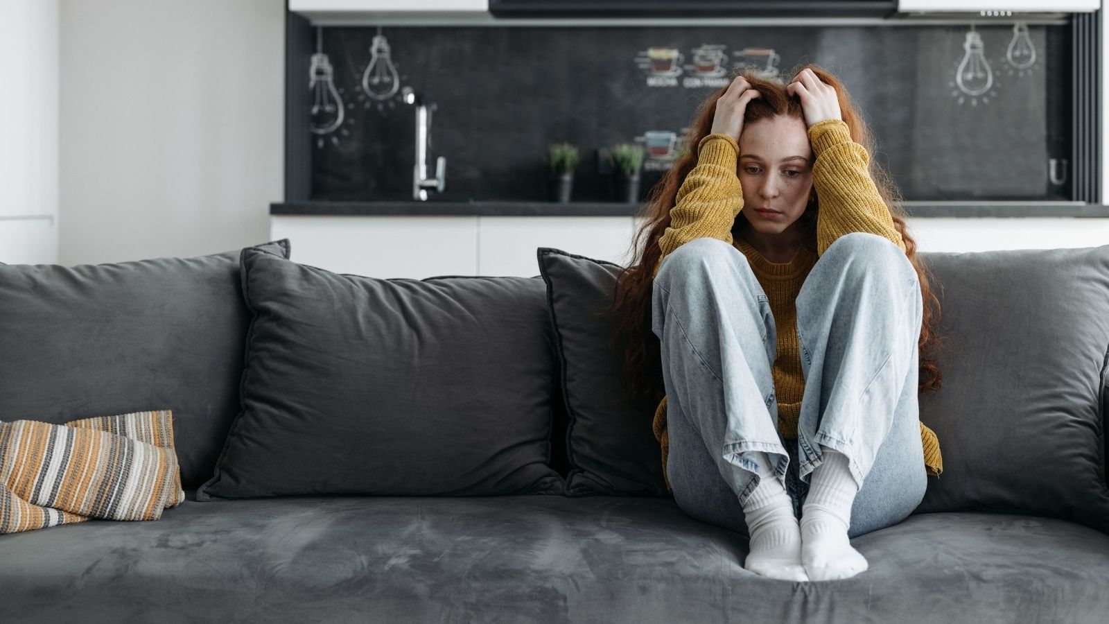 She Moved Into A Neighborhood That Seemed Quiet, But Months Of Howling Dogs At 6 AM And Late Night Garage Music Have Her Ready To Rent Out Her House And Leave Woman sitting on her couch stressed over neighbor noice