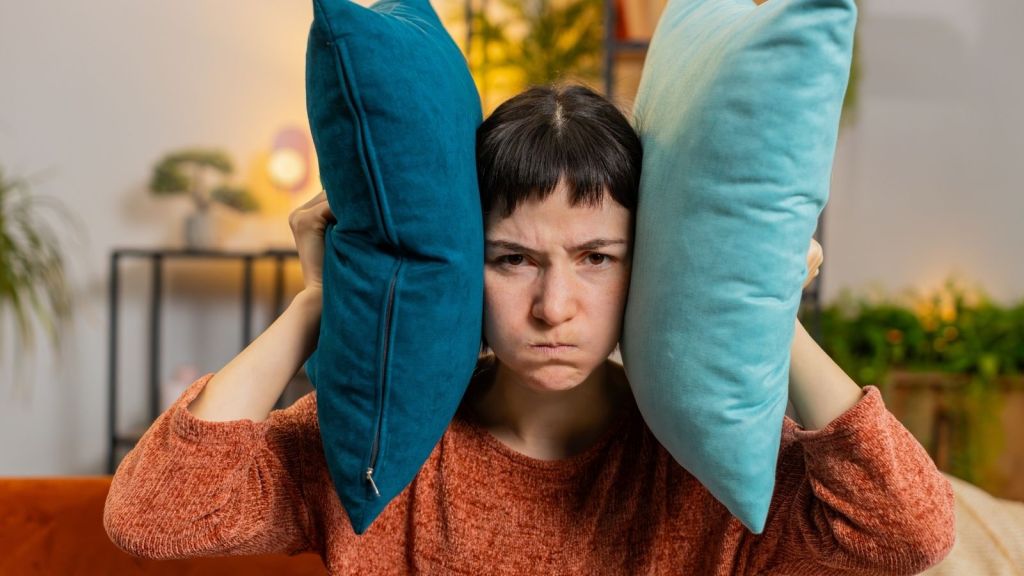 upset woman covering her ears with pillows