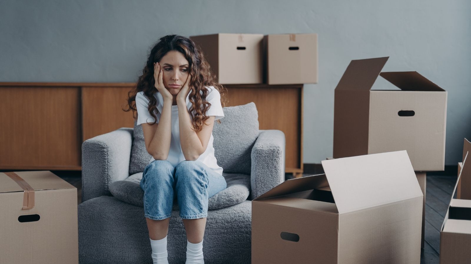 She Spent $6,000 on Medical Bills and Ruined Wardrobes After Her Neighbor Sprayed Industrial Solvent Under Her Door—Then Court Dismissed Her Protective Order for Lack of Direct Physical Proof sad woman surrounded by moving boxes