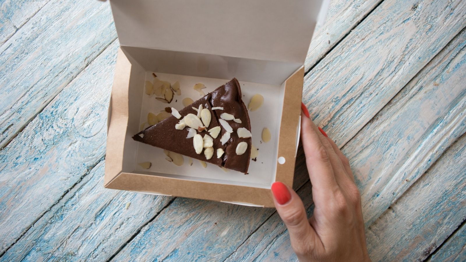 woman's hand on a takeout box containing a slice of chocolate cake