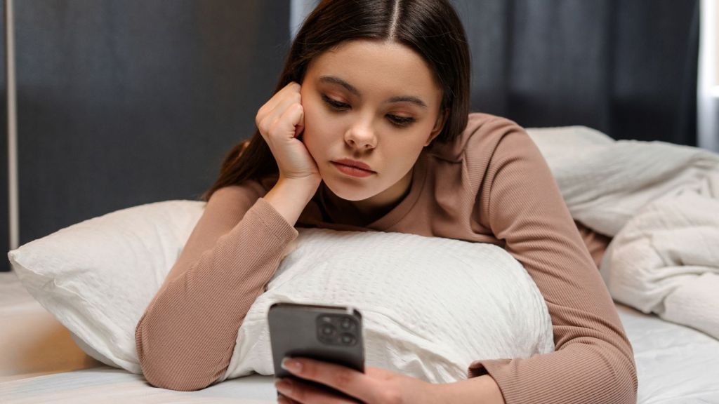 sad teenage girl looking at her phone in bed