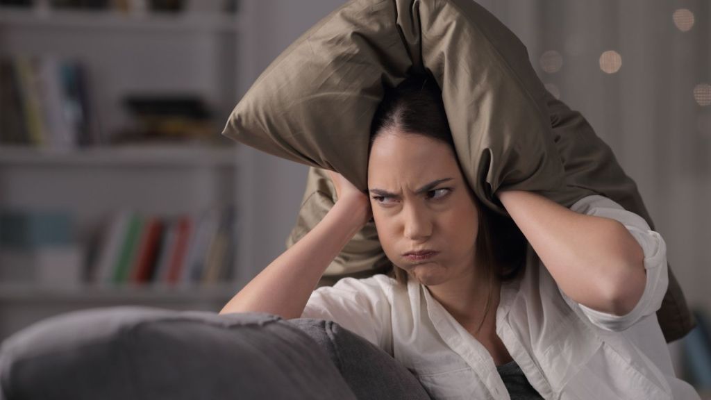 frustrated woman covering her ears with a pillow