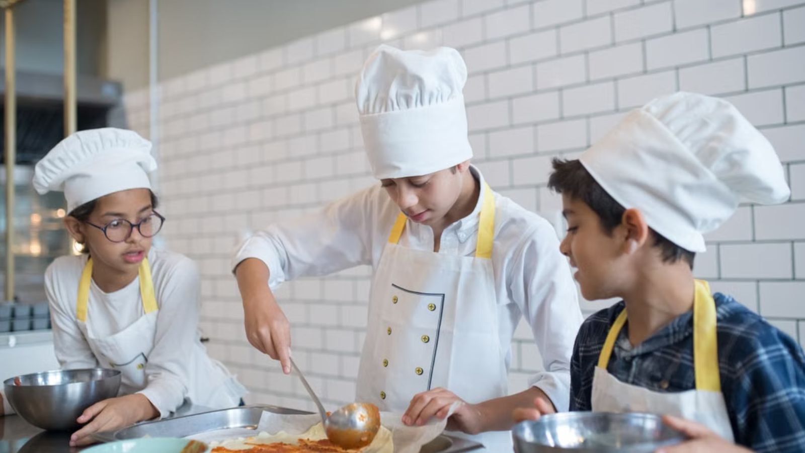 Kids wearing chef uniforms preparing food in the kitchen