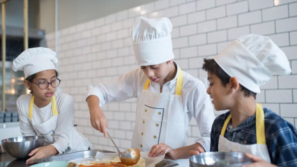 Kids wearing chef uniforms preparing food in the kitchen
