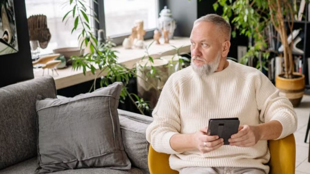 Elderly man sitting with smartphone and gadgets in a modern living room
