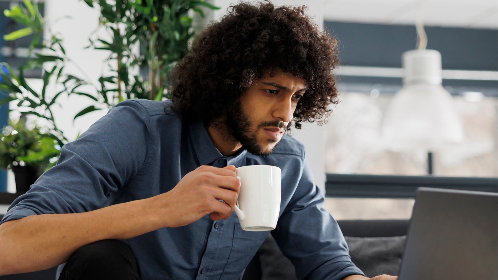 Man holding a cup with one hand and intently looking at his laptop