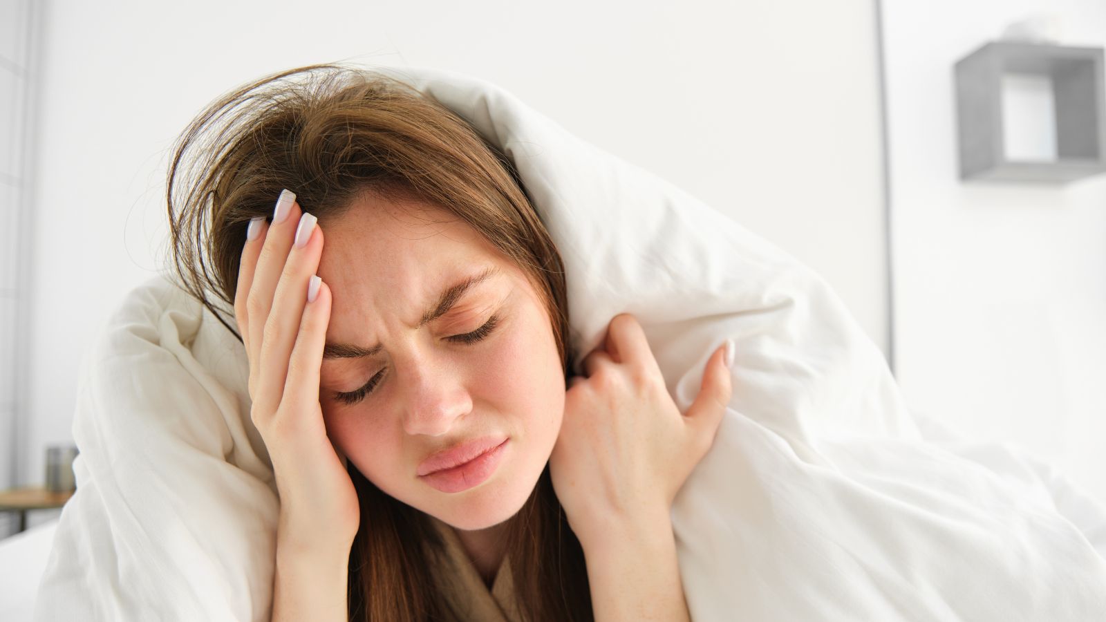 Woman covering herself with white blanket and feeling frustrated