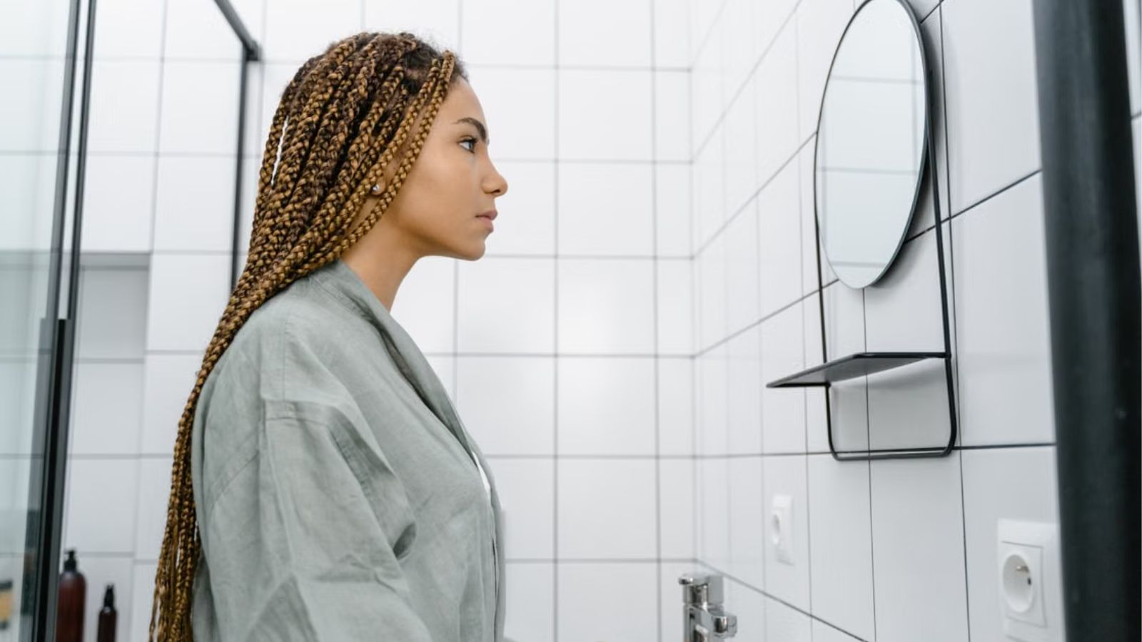 She Asked Her Roommate to Limit Her Two Hour Morning Bathroom Hold Up—Then Got Into a Furious Argument Over Clogged Drains and Hair Extensions Woman with braided hair looking at the mirror in the bathroom