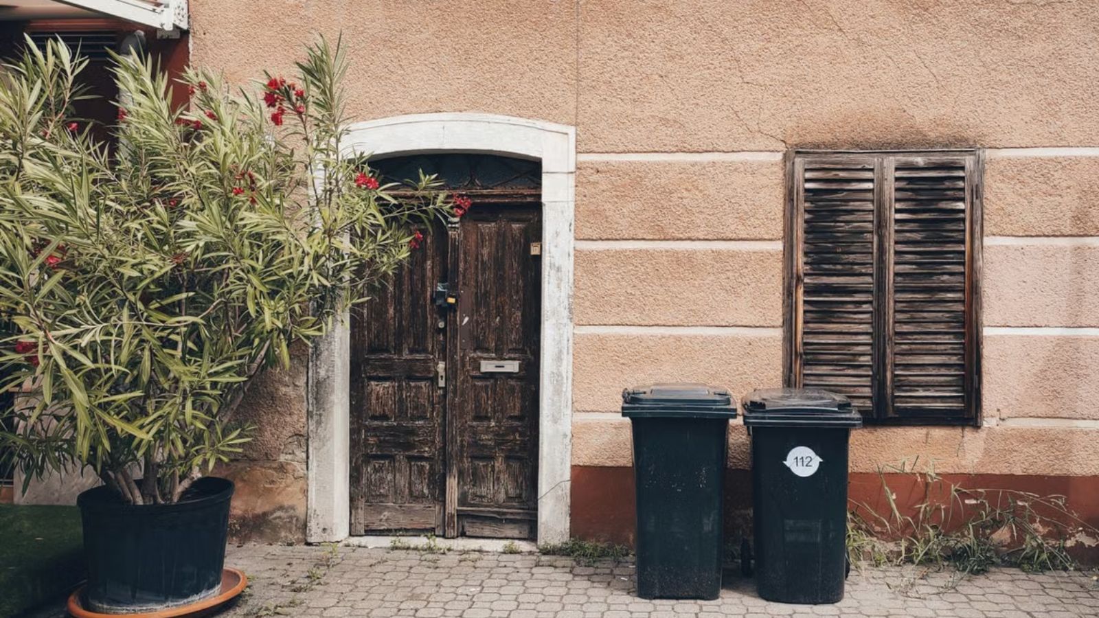 Two black garbage bins placed in front of a house and near the door