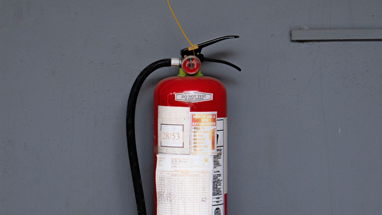 A fire extinguisher placed against a gray wall