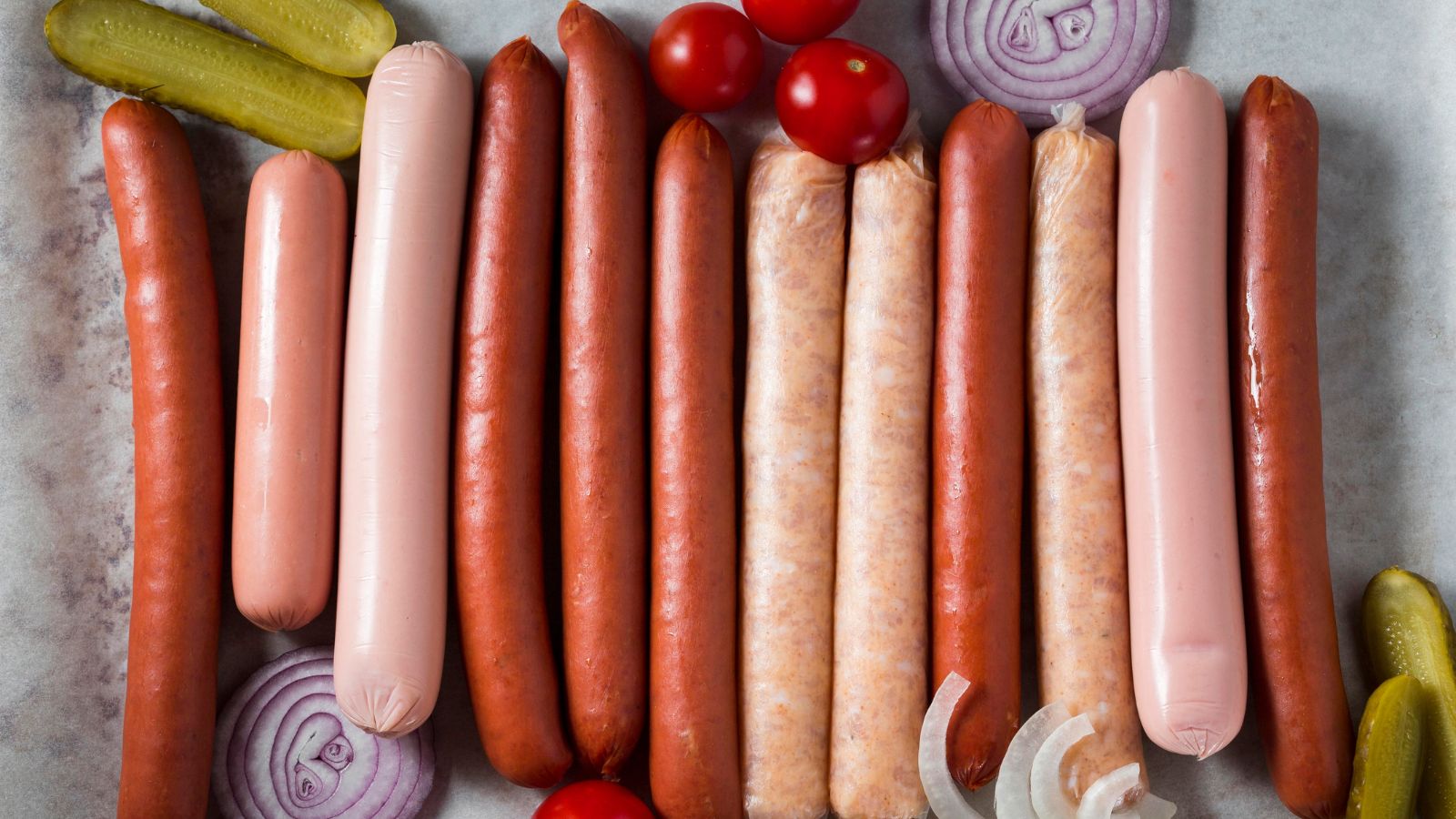 Man Defrosted Sausage In The Microwave Without A Plate, So His Wife Worried He Was Contaminating The Kitchen Different kinds of sausages lined up on the kitchen counter with onions and tomatoes