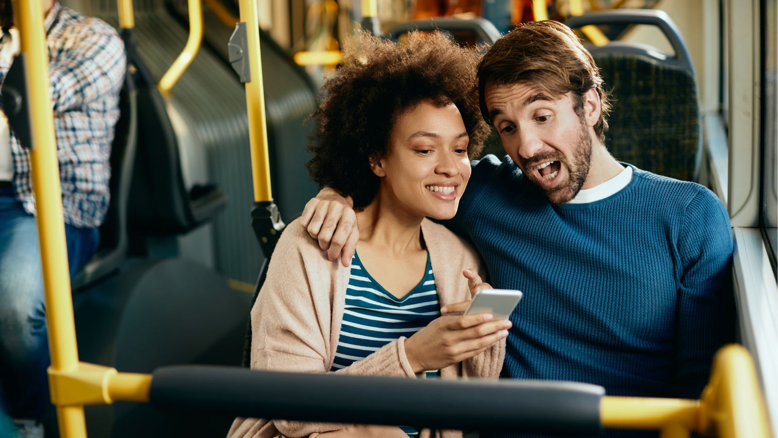 She Was Just Talking With Her Husband on a Greyhound Bus — Another Passenger Demanded They Stop So She Could Sleep Man and woman sitting close to each other on a bus and looking at a phone