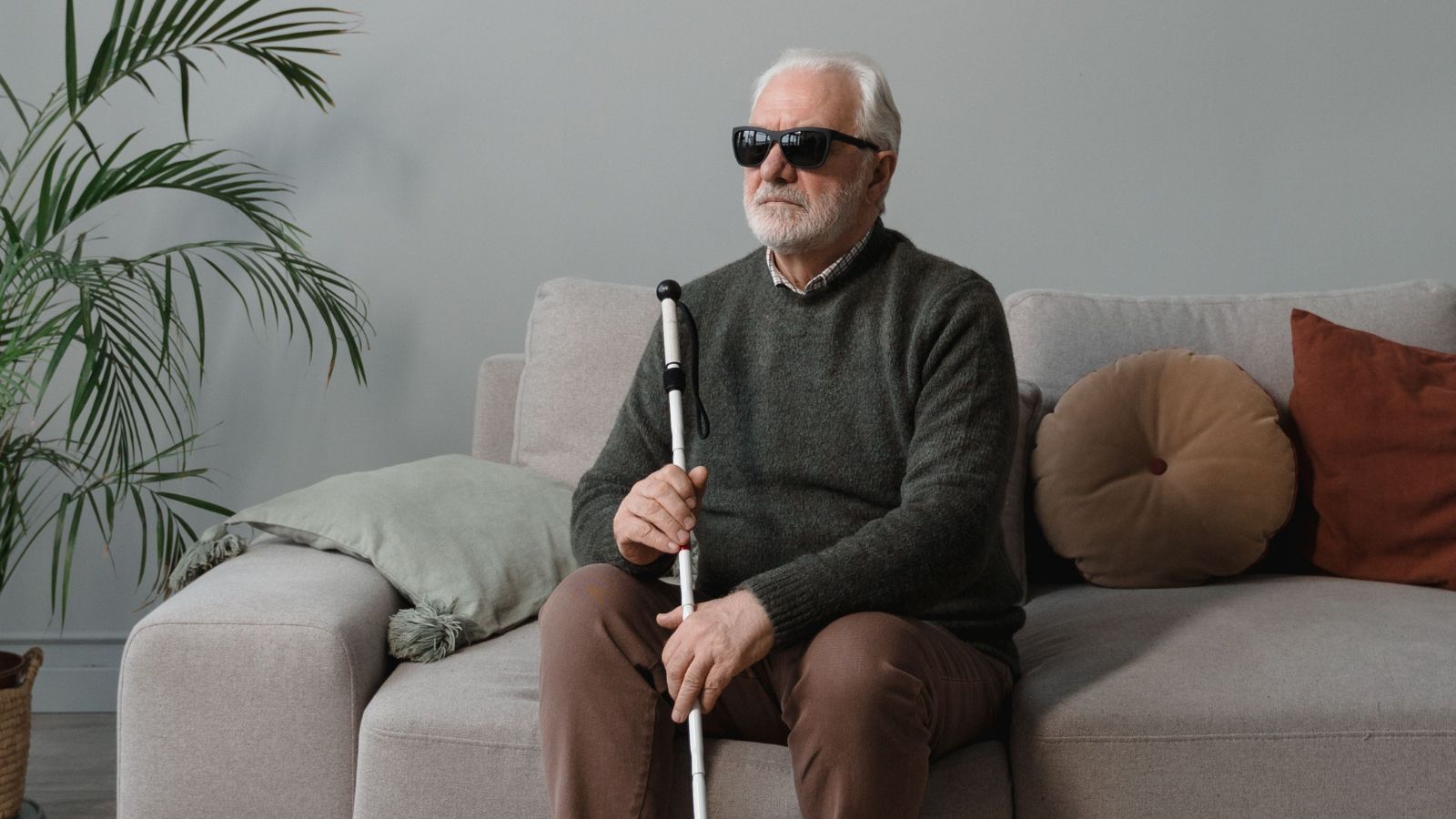 Blind old man sitting on the couch with eyeglasses and stick