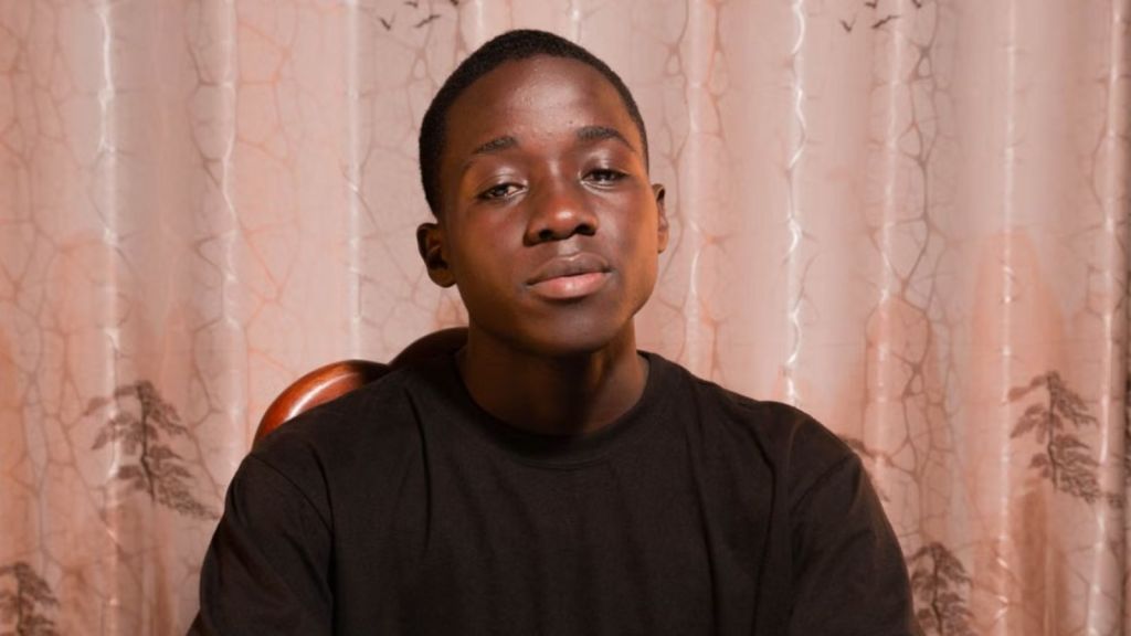 A young man sitting at a table indoors with a neutral background