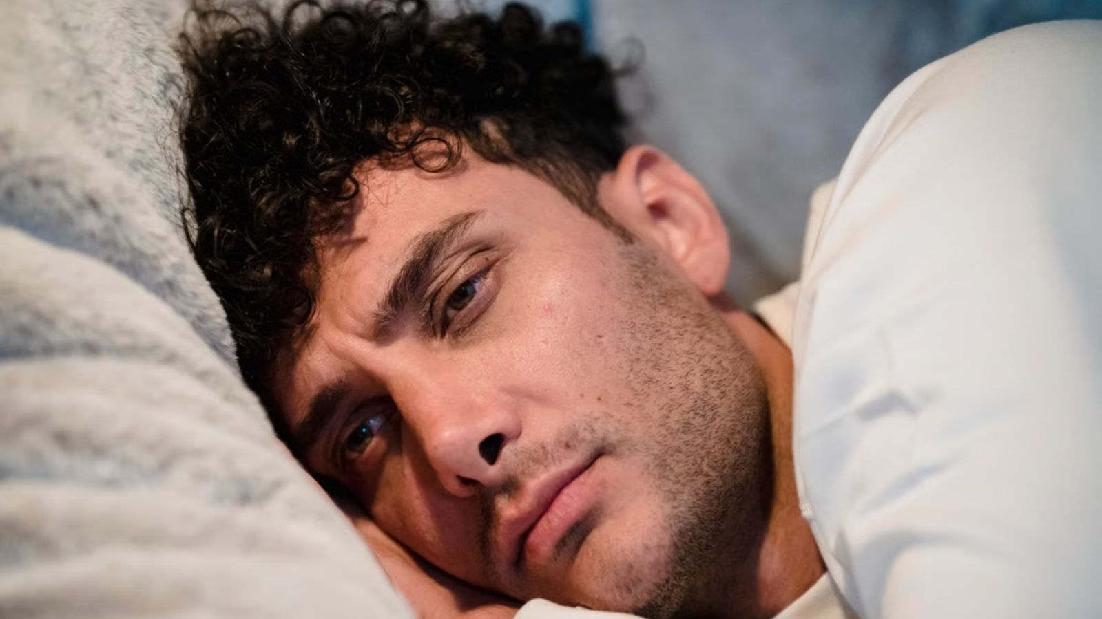 Man Tried To Stay Quiet In His Condo, But His Downstairs Neighbors Subwoofer And Ceiling Fan Kept Disturbing Him Man lying on the bed but couldn't sleep