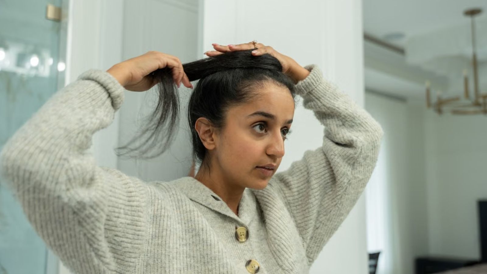 Young woman tying her hair while looking at a mirror
