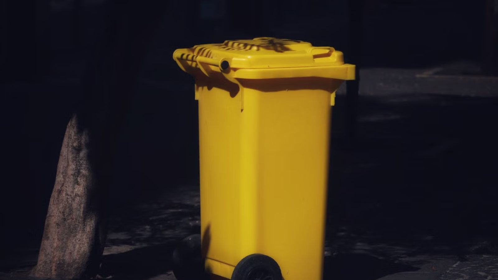A big, yellow trash bin outdoors at night