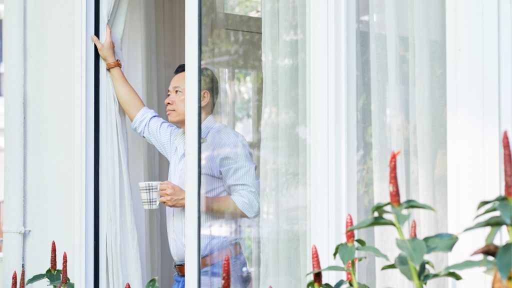 Man looking out the open glass sliding door while holding a mug