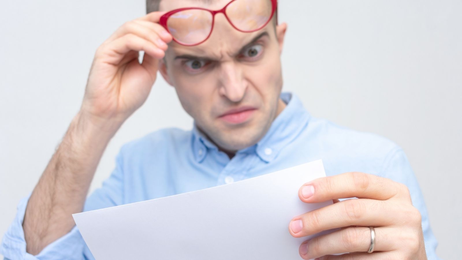angry man raises his glasses while reading a letter
