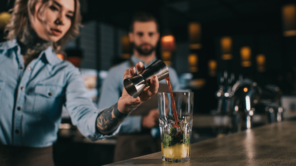 bartender adding ingredients with other bartender looking on