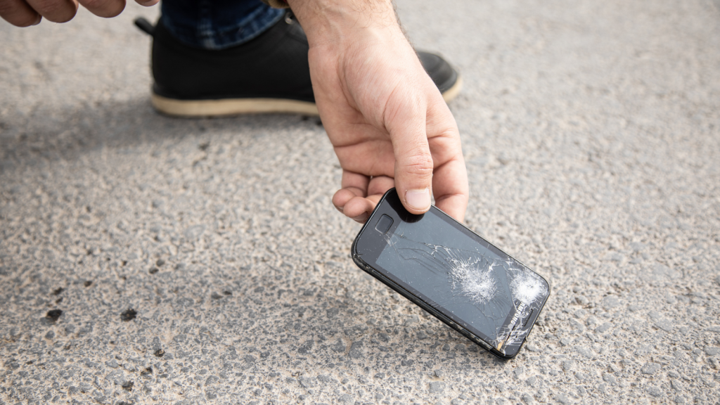 She Replaced Her Teen’s Destroyed iPhone 15 Pro for $1,200—Then Discovered It Was Only a $30 Cracked Screen Protector closeup of a person picking up a phone with a broken screen