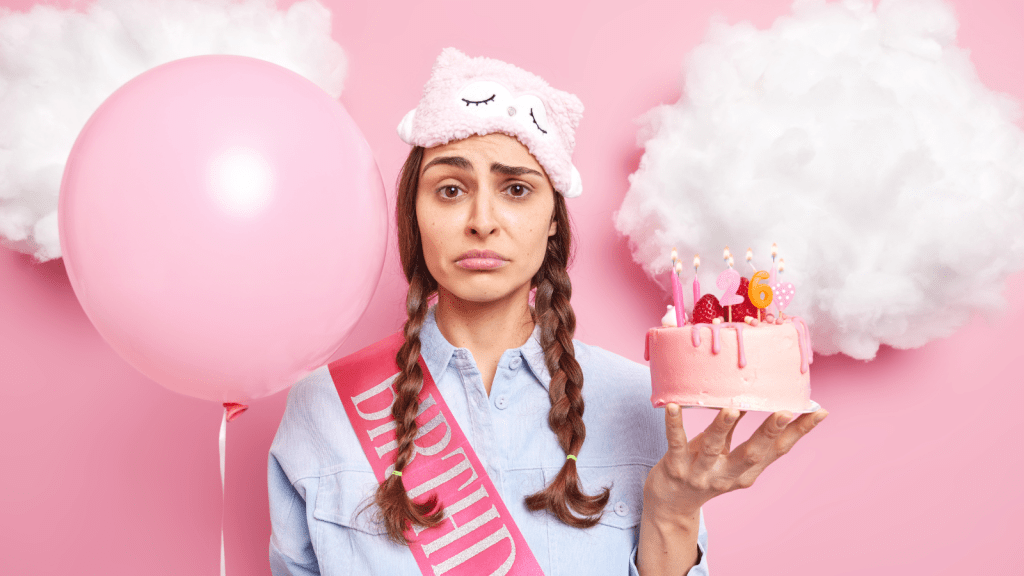 She Asked for a Low Key Birthday to Focus on School — Her Partner Threw Her a Surprise Party Anyway displeased young woman holding birthday cake and decorations