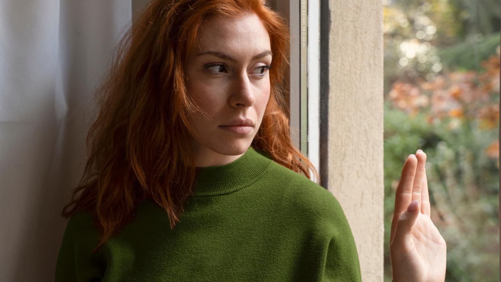 Woman Is Nervous About Her Husband Leaving For A School Program Because Her Neighbor Is Unpredictable And Aggressive woman looking out a window