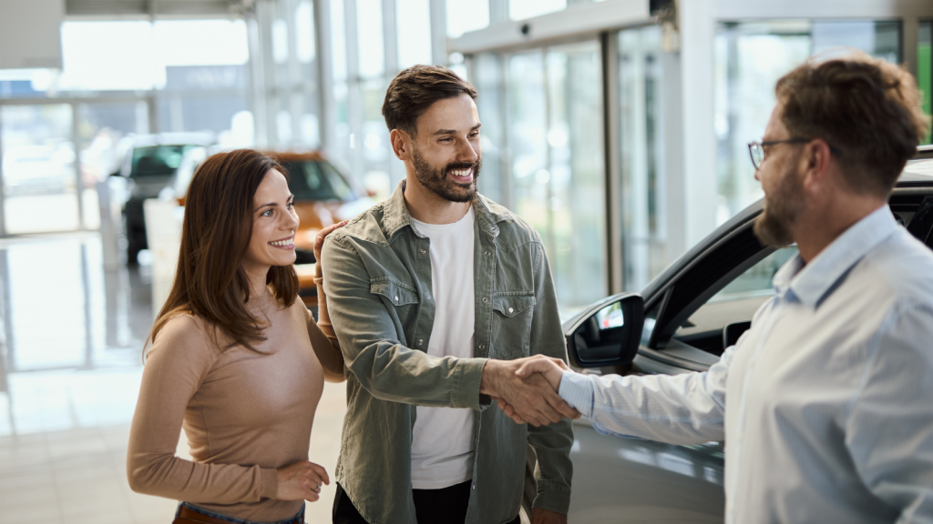 happy young couple buying car shaking dealer hand