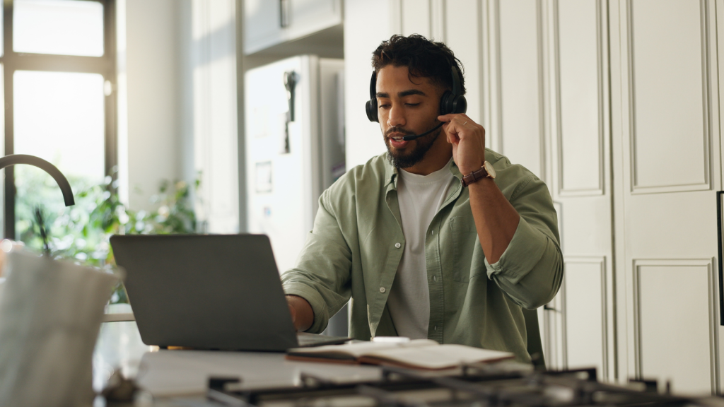 man on laptop with headphones and microphone working in kitchen