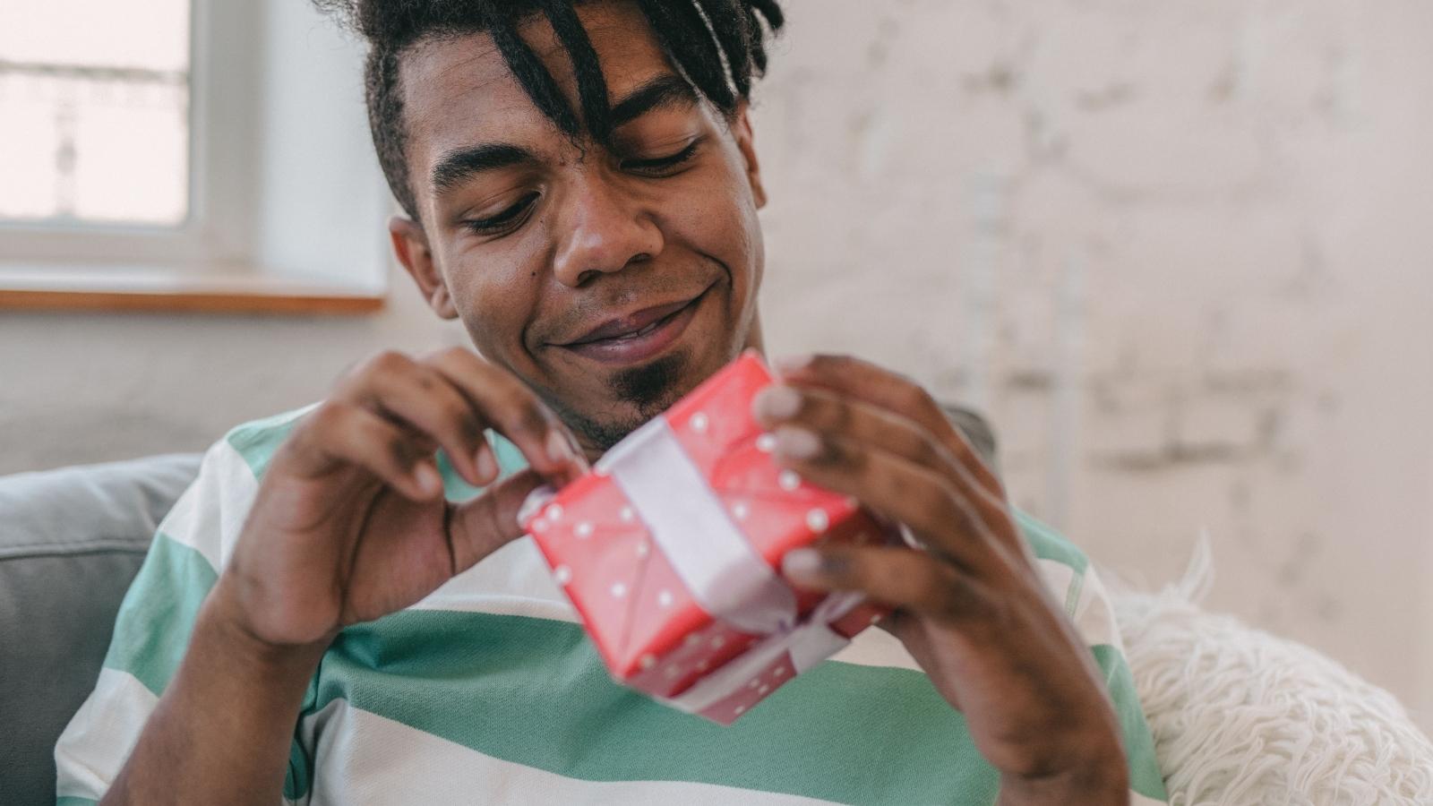 Boyfriend Saved For Months To Buy The Exact Headphones His Partner Wanted, But She Said The Gift Wasnt Good Enough man opening a gift in red wrapping paper