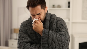 Brother Hoped For A Peaceful Vacation, But His Sibling’s Reckless Behavior Left Him Sick And Wondering Whether He Should Distance Himself Completely sick man wrapped in a blanket sneezing into tissue