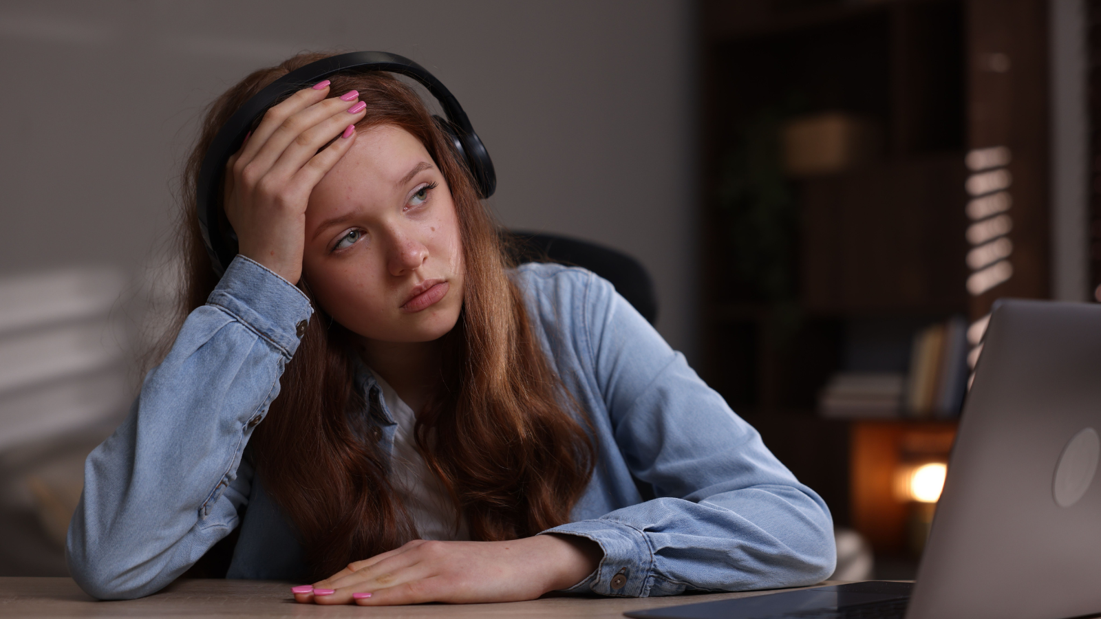teen girl with headphones on and head in hand looking sad