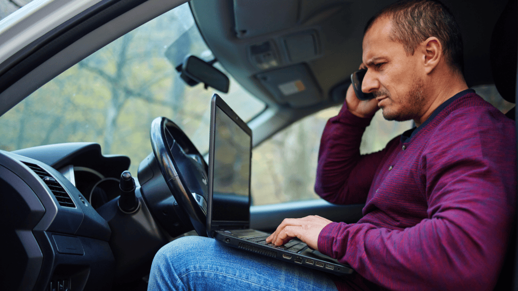 Man sitting in a car working on a laptop