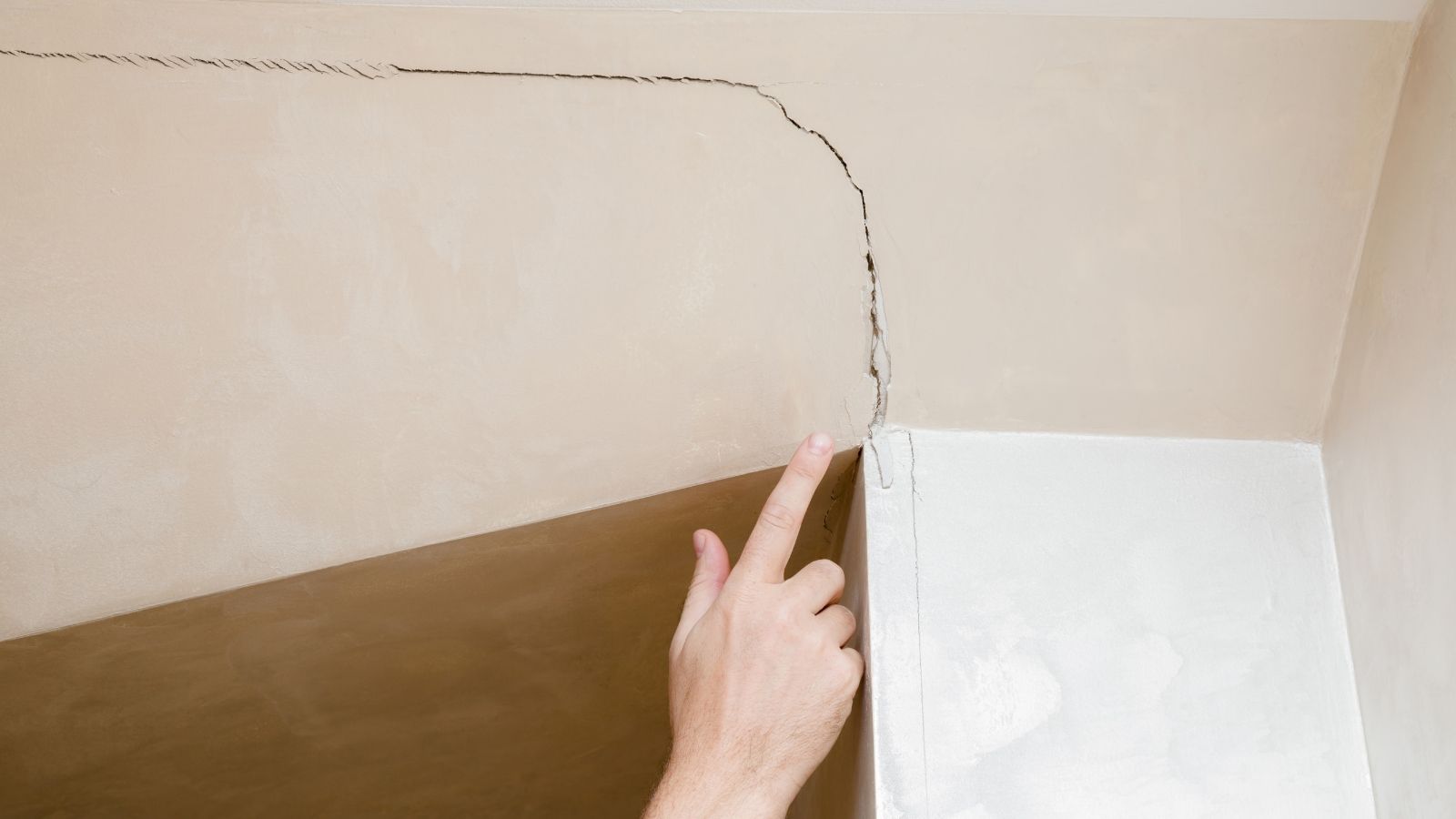 A Tenant Flagged Escalating Cracks and Structural Shift—Only for the Property Manager to Dismiss It as Cosmetic Settling hand pointing to a crack in a wall